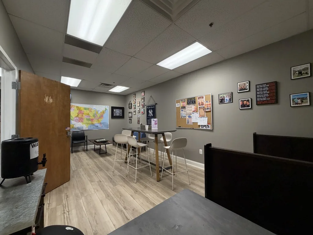 The real lounge inside BB's Bagels: gray walls, a bulletin board, framed photos, a high-top table with white stools, and a dark booth